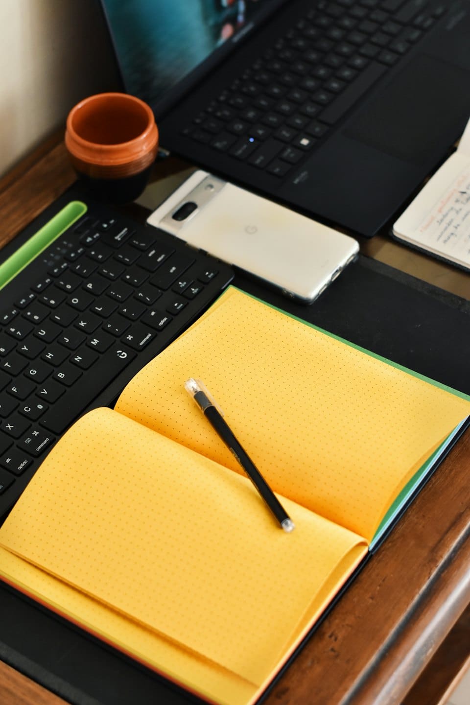 Portátil, teclado y cuaderno sobre un escritorio de madera.
